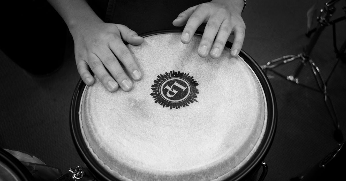 A black and white close-up shot of hands drumming on a bongo drum, emphasizing rhythm and music.